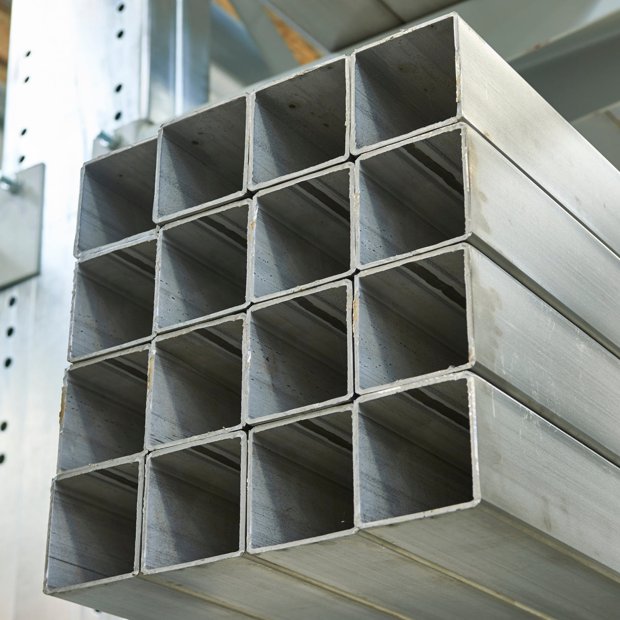 Stos kwadratowych profili nierdzewnych ułożonych na metalowym regale magazynowym.