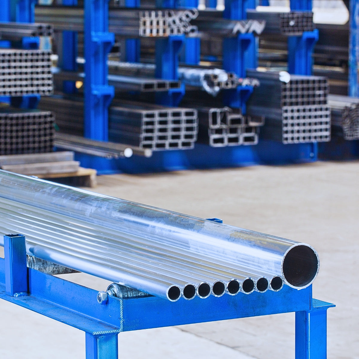 Rury aluminiowe ułożone na regale w hurtowni aluminium – widok z hali z regałami i profilem okrągłym na pierwszym planie.