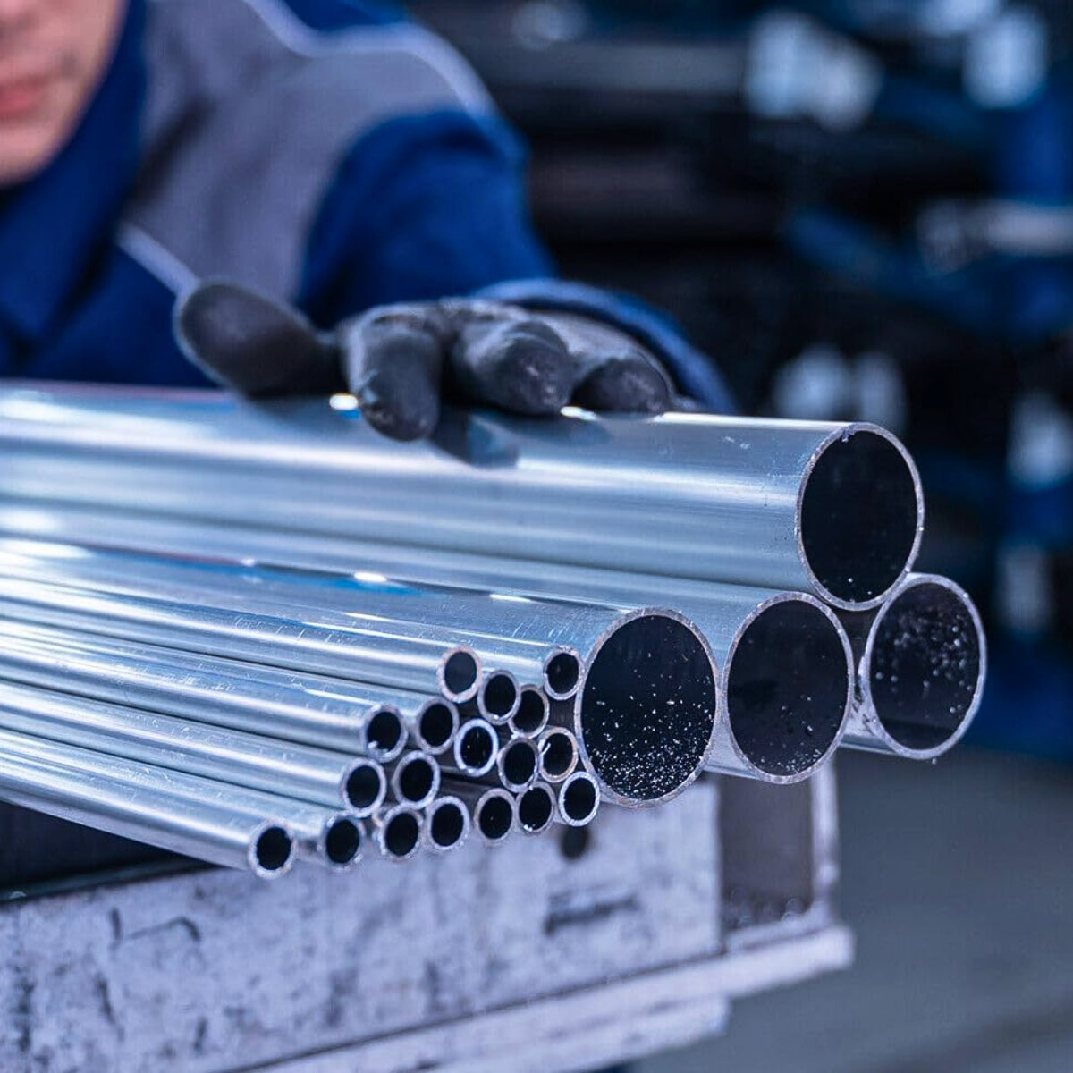 Rury aluminiowe przygotowane do cięcia i obróbki w hali przemysłowej – widoczna ręka pracownika chwytająca rurę